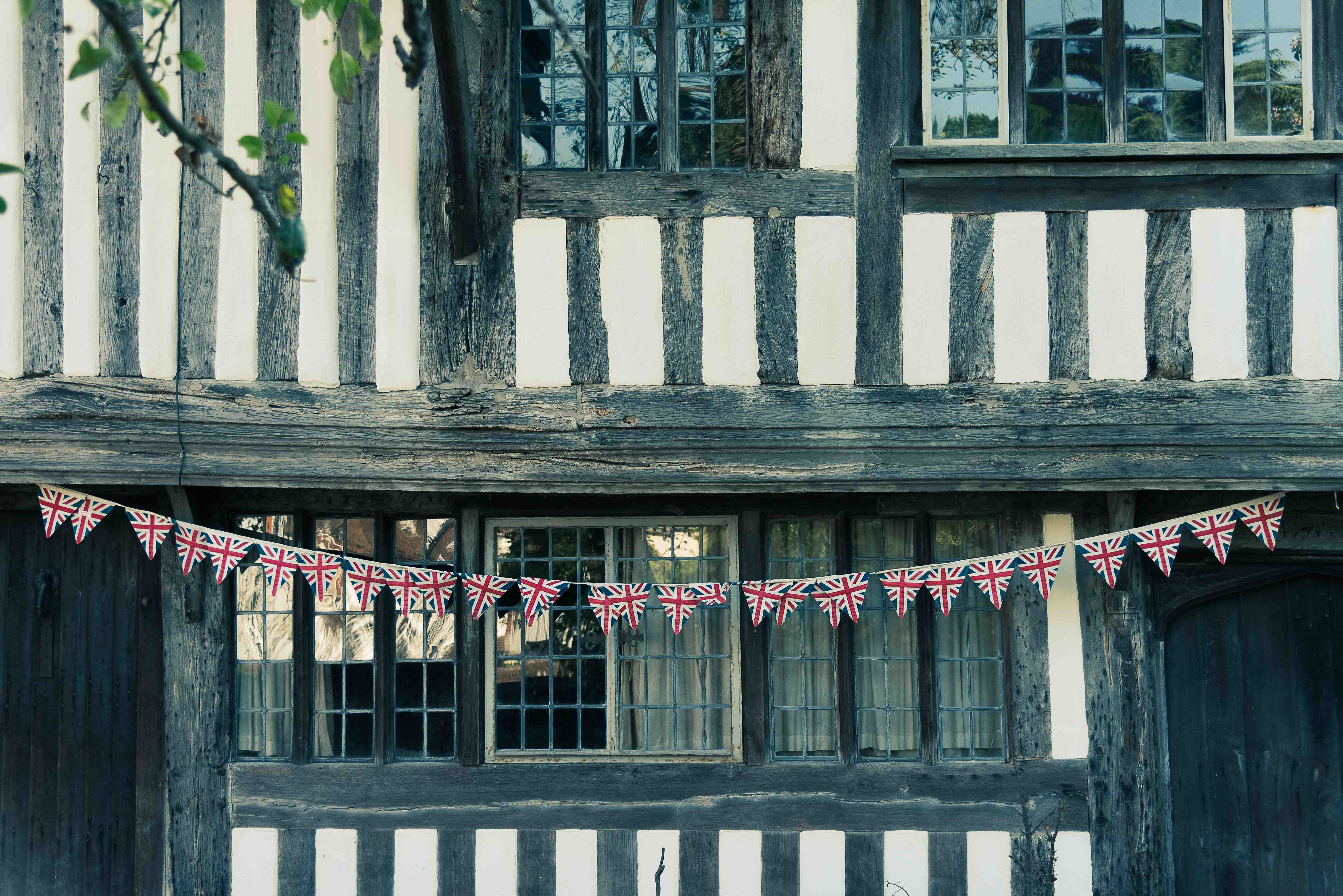A close-up of a traditional English cottage featuring black and white timber framing, adorned with hanging bunting displaying the Union Jack flags.